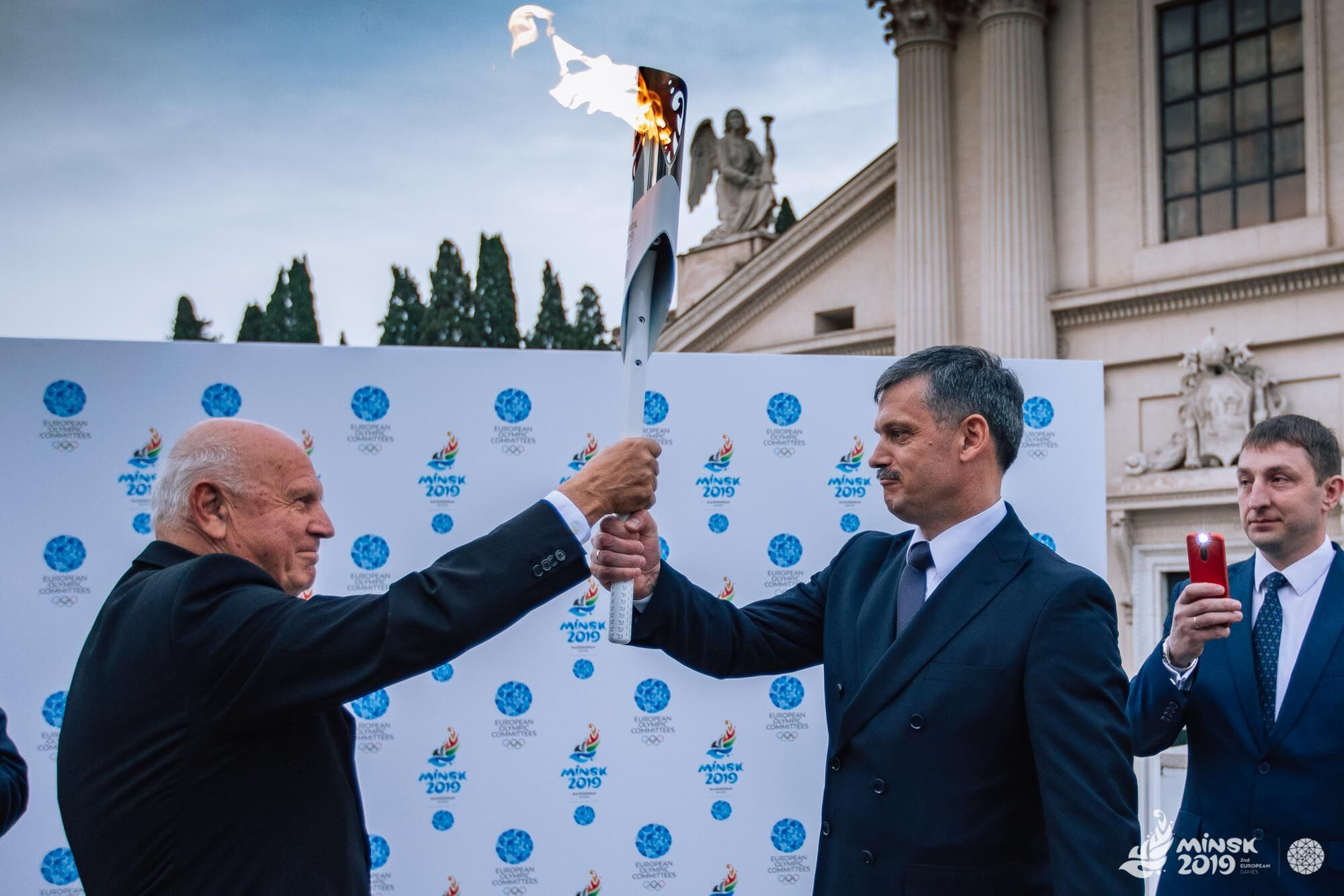 European Olympic Committees President Janez Kocijančič, left, helps to hold aloft the Flame ©Minsk 2019