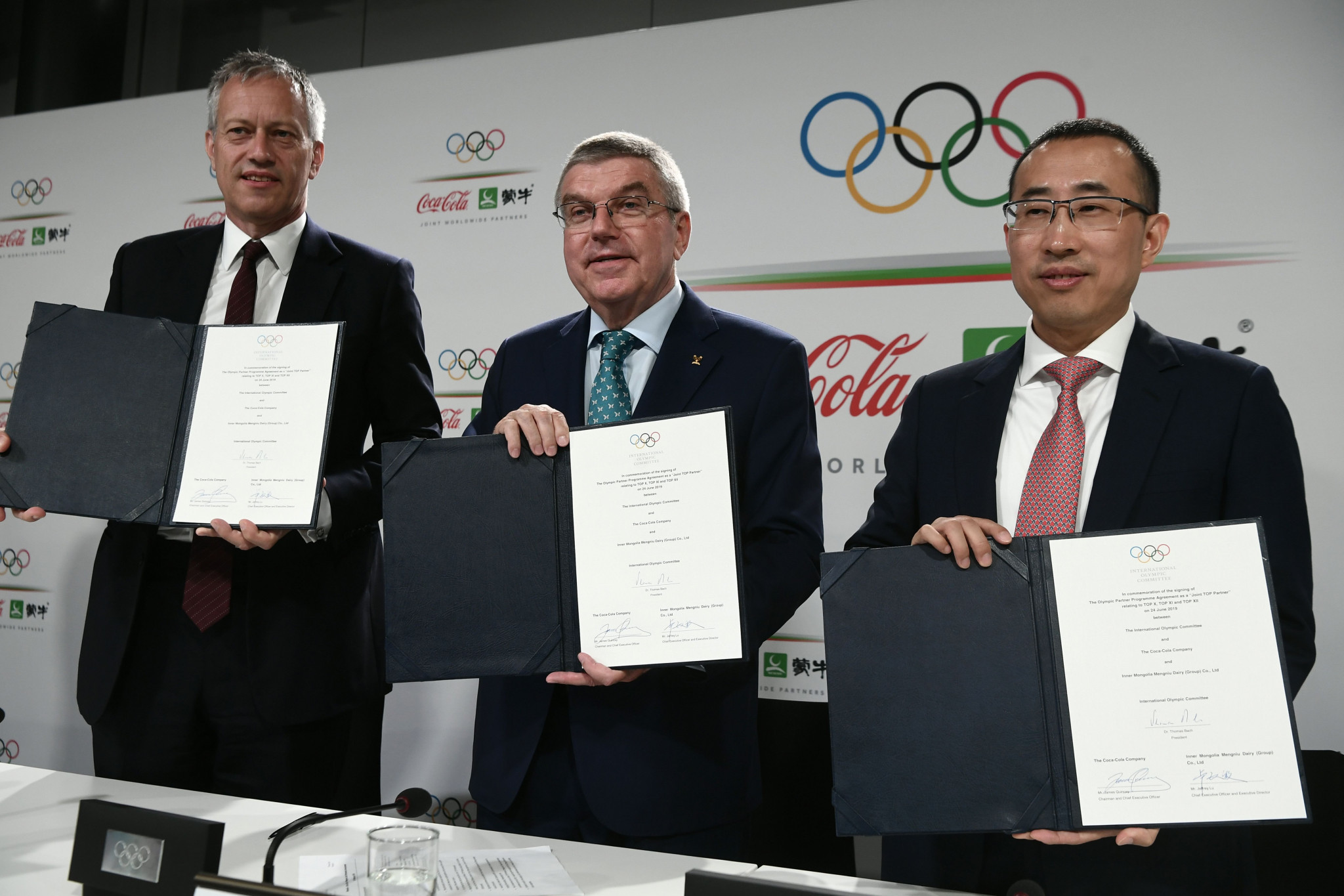 IOC President Thomas Bach, centre, shows off the newly-signed contract with Coca-Cola chief executive and chairman James Quincey, left, and Jeffrey Lu, chief executive of Mengniu, right ©Getty Images