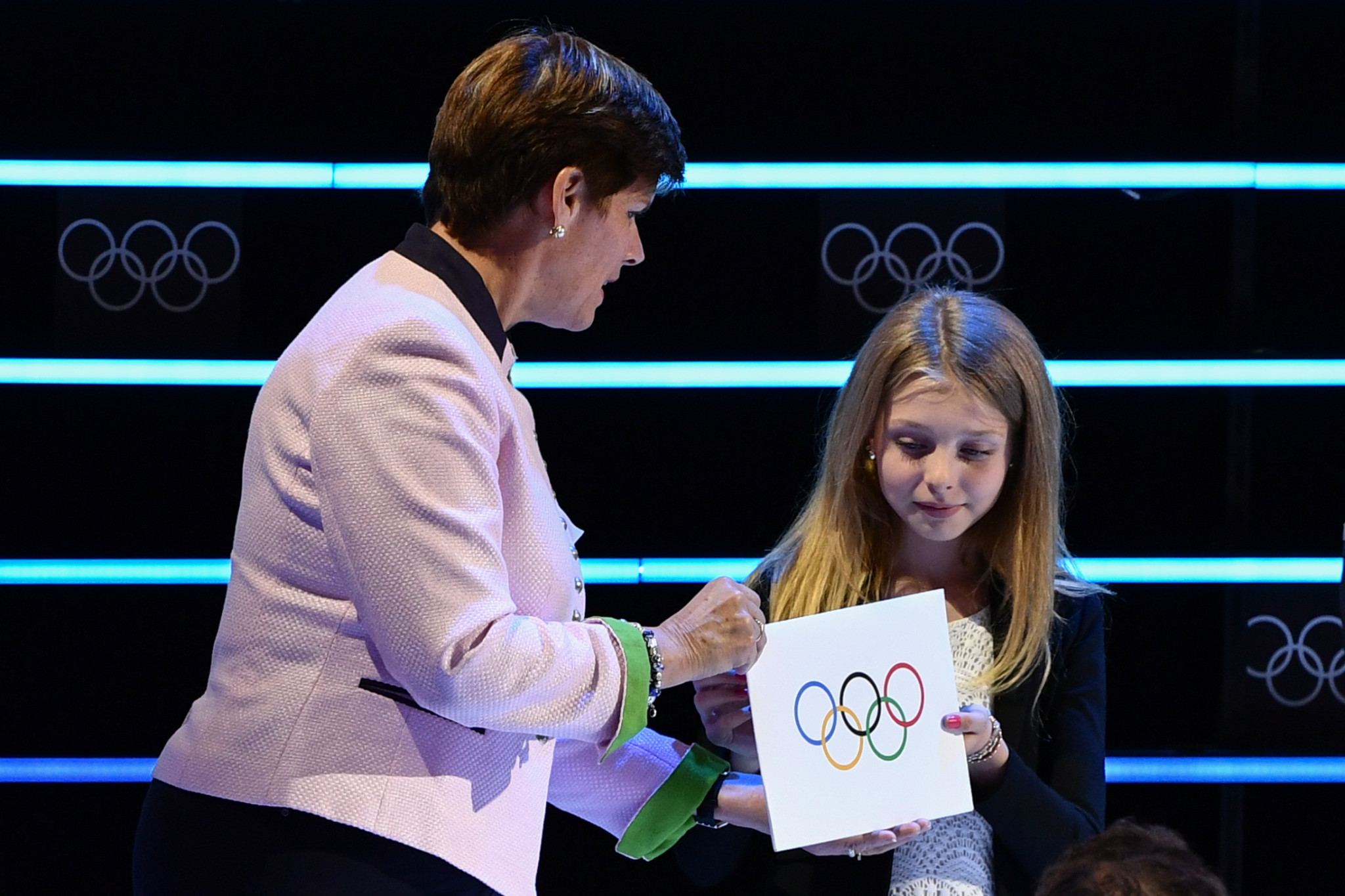 Nicole Hoevertsz gives the envelope containing the name of the winner of the 2026 Winter Olympics to 10-year-old Livia de Bon, a figure skater from Lausanne, who in turn passed it to IOC President Thomas Bach ©Getty Images
