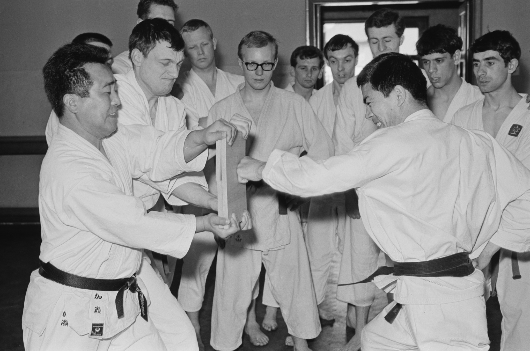 Japanese teacher of Shotokan karate Hirokazu Kanazawa demonstrating the breaking of a piece of wood in front of a group of students, UK, 2nd May 1965 ©Getty Images
