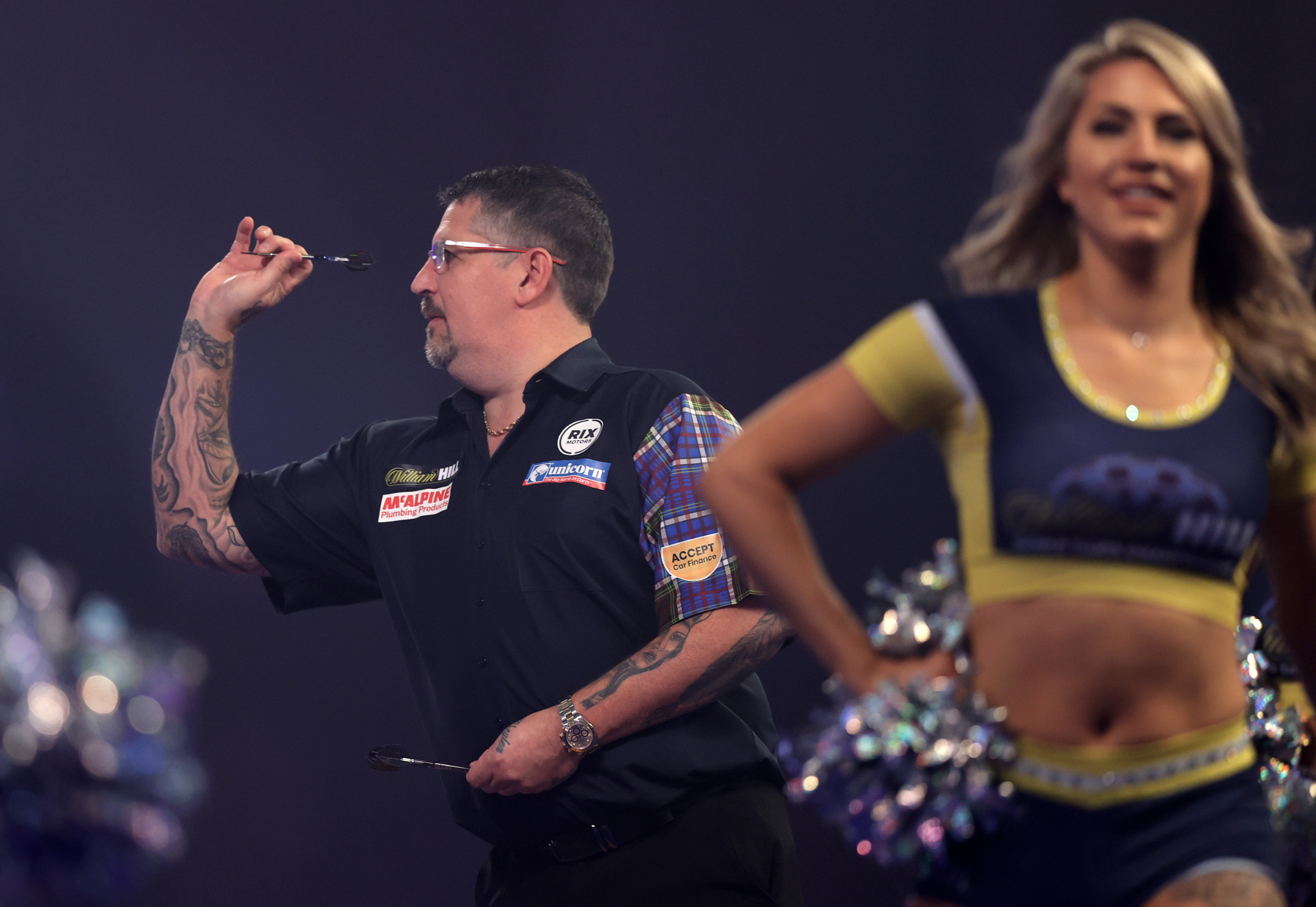 Gary Anderson in action at the PDC World Darts Championship as a cheerleader leaves the stage ©Getty Images