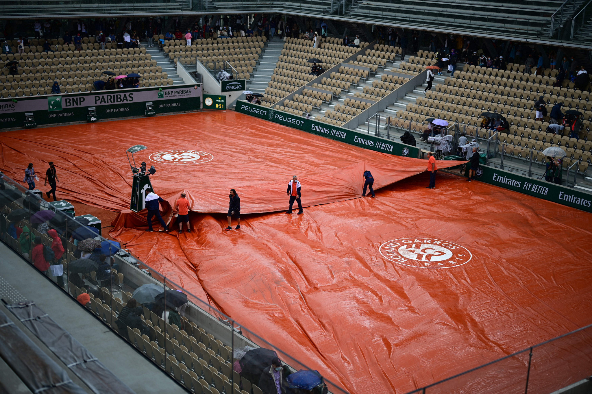 Groundstaff members pull covers across the Simonne Mathieu court as rain falls ©Getty Images