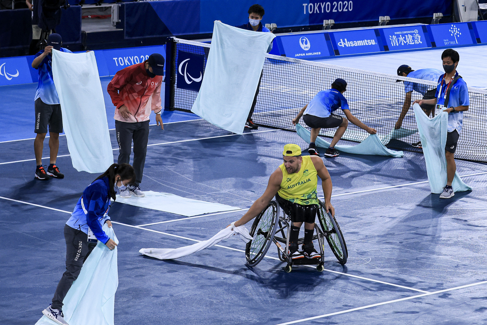 Australia's Dylan Alcott lends a hand as volunteers dry the courts at the Ariake Tennis Centre before his men's quad doubles wheelchair tennis gold medal match ©Getty Images