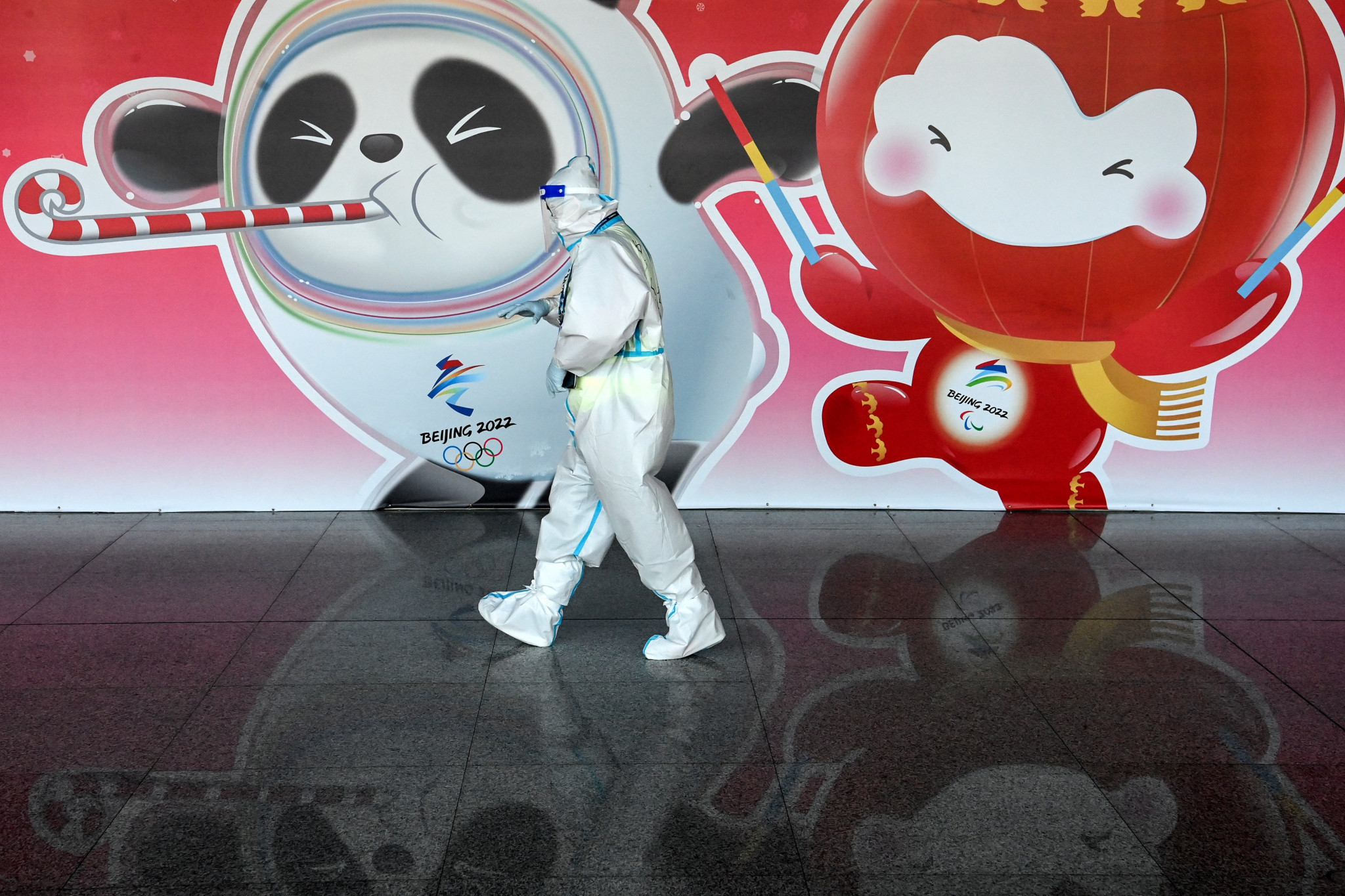 An airport worker, wearing an hazmat suit, walks past an Olympic mascot banner at the Beijing Capital International Airport ©Getty Images