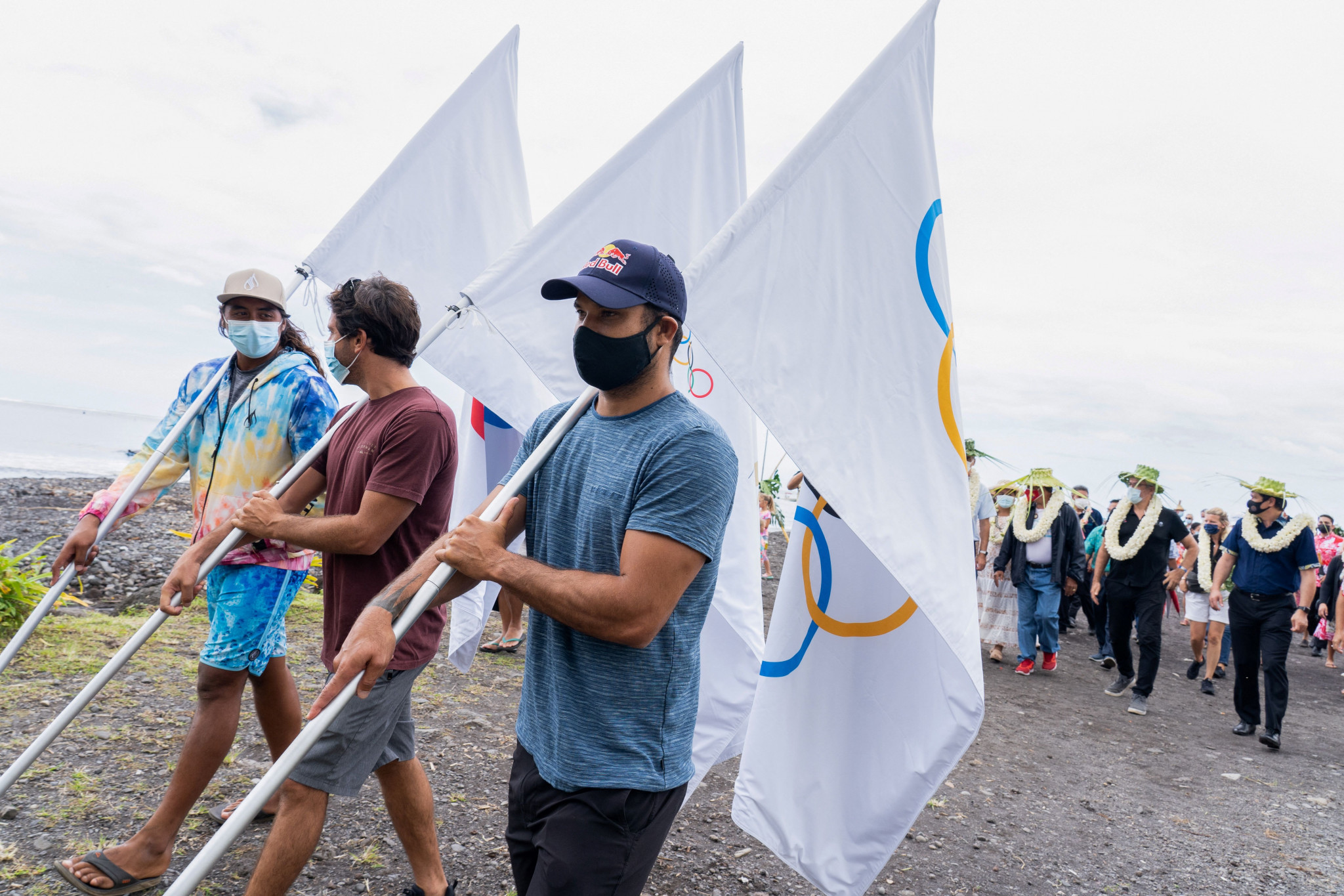 The Tahitian Matehau Tetopata, a young local surfer from Teahupo'o, left, the Reunionese Jeremy Flores, centre and the Tahitian Michel Bourez, right, walk and hold the three Olympic flags as they attend a cultural ceremony organised by the population to w