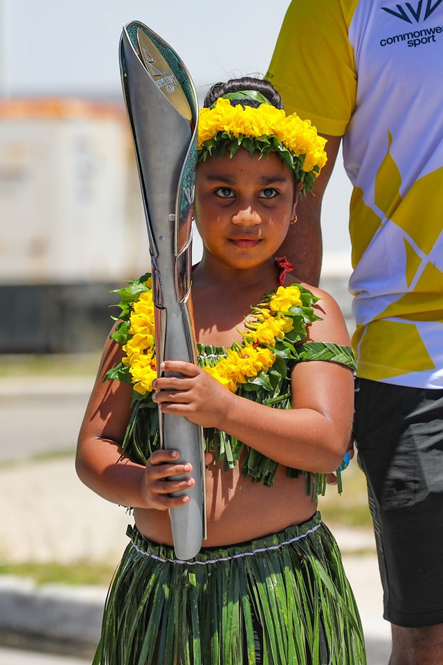 A child wearing a grass skirt holds the Baton during its visit to Nauru ©Birmingham 2022 