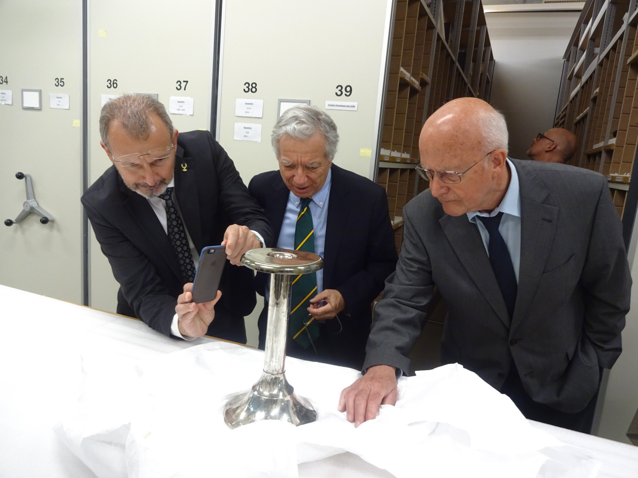 Olympic historians Kostas Georgiadis, David Wallechinsky and Volker Kluge examine an original Olympic Torch in the vaults of the Olympic Museum ©ITG