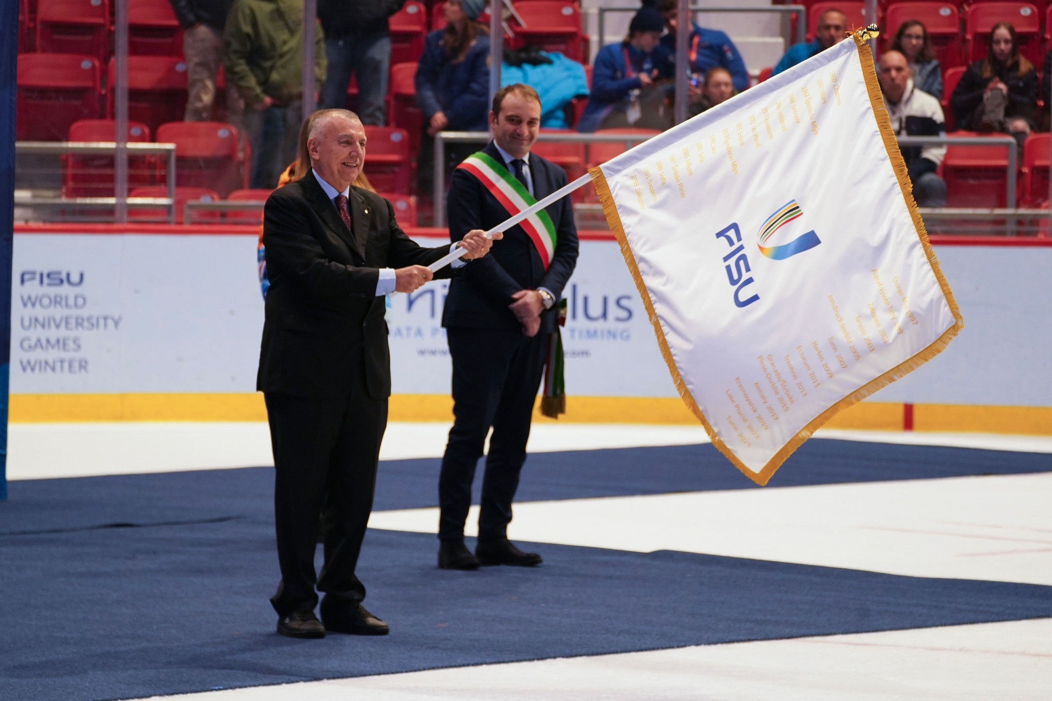 Lornezo Lentini, vice-president of Turin 2025, waves the FISU flag as Turin Mayor Stefano Lusso watches on ©FISU