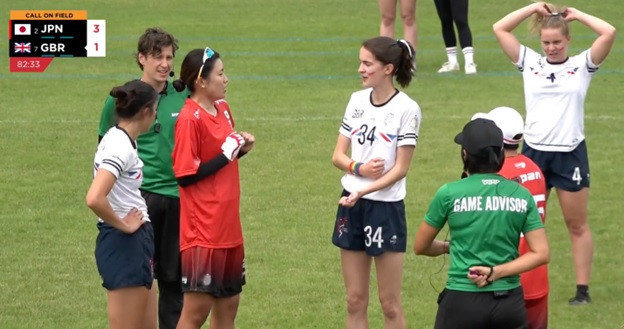 Britain's Katie Trim, centre in white, and Japan's Yui Nishide, centre in red, discuss an incident during the match while the game advisors stand by ©WFDF