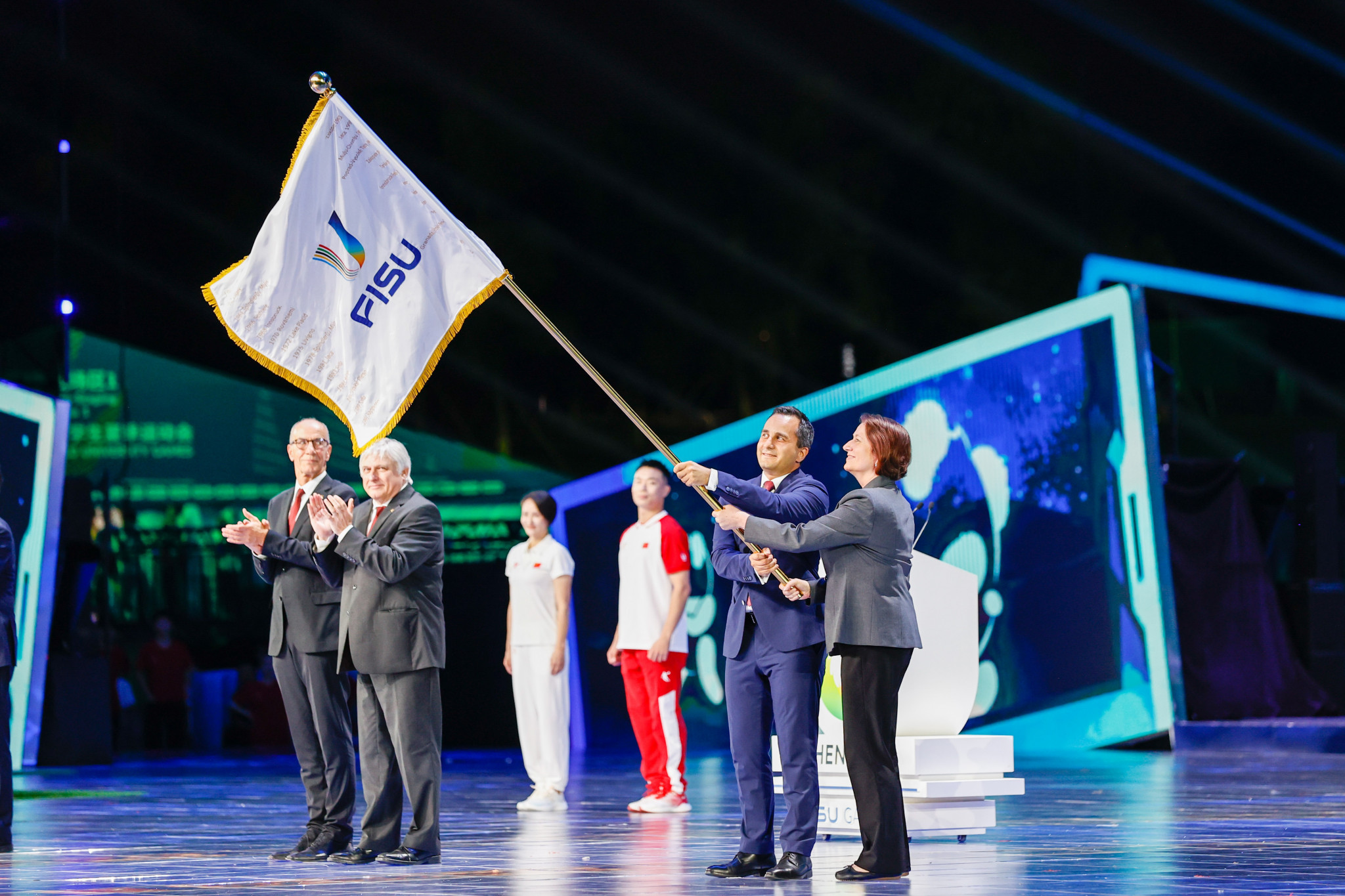 The FISU flag is waved by Mahmut Özdemir, Secretary of State in Germany’s Ministry of Interior and Community, and German FISU Executive Committee member Verena Burk, after it had been passed to Rhine-Ruhr 2025 at the end of Chengdu 2021 ©Rhine-Ruhr 2025