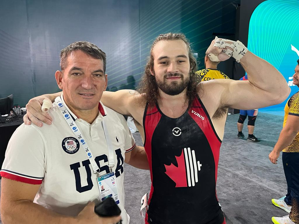 Boady Santavy of Canada, right, celebrates with triple Olympic champion Pyrros Dimas after making his first lift in international competition since December 2021 ©IWF 