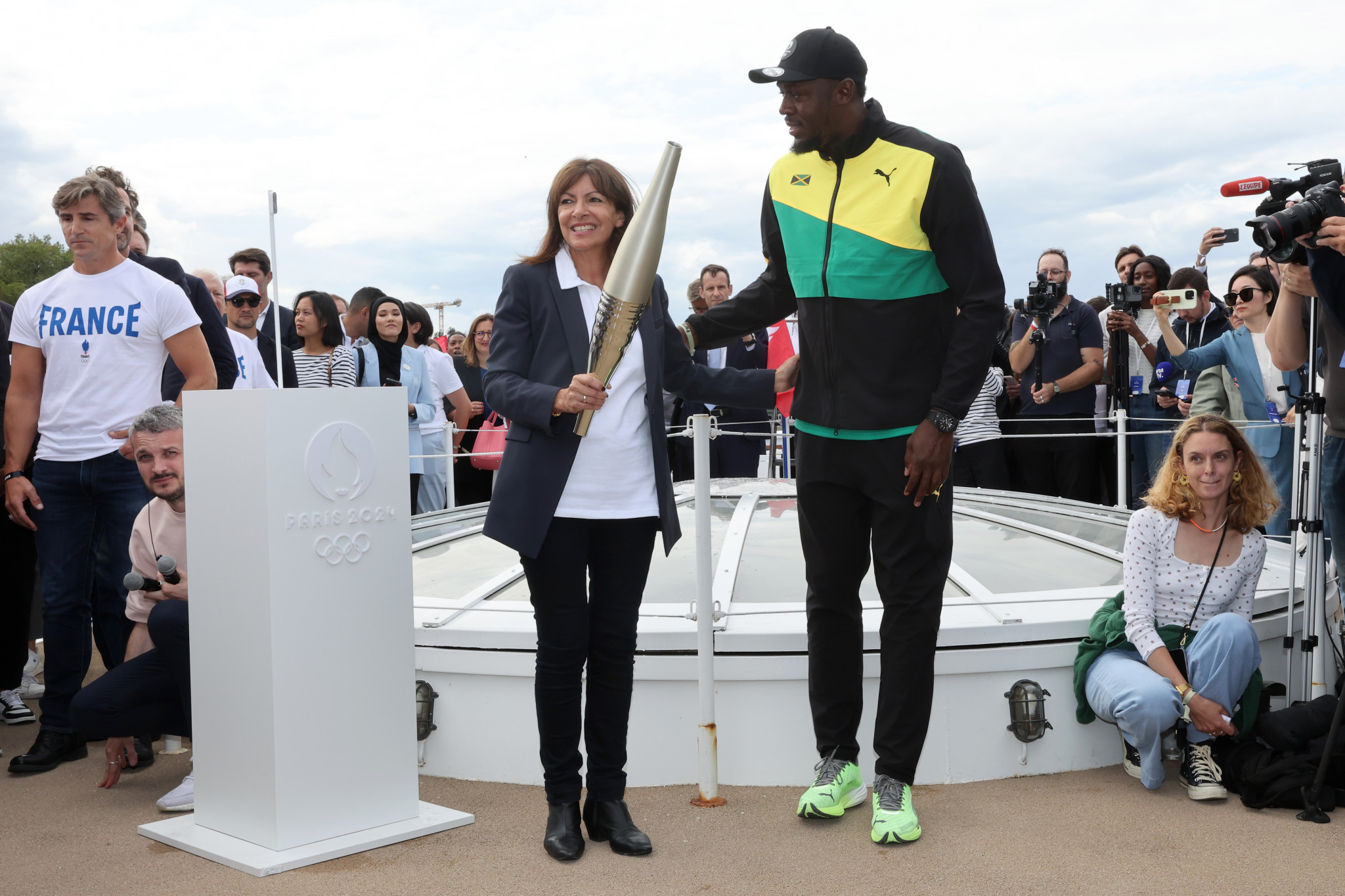 Paris Mayor Anne Hidalgo holds the Olympic torch next to Former sprinter Usain Bolt during a Pre-Olympic tour along the Seine with the Eiffel Tower in the background © Getty Images