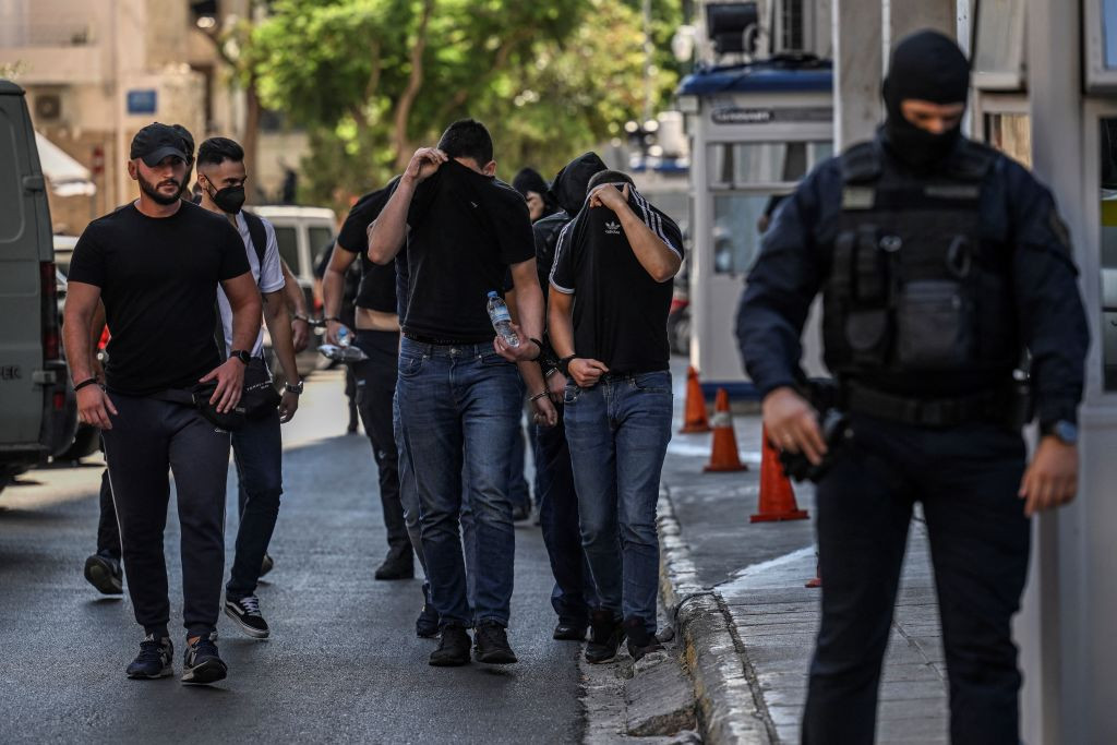 Football fans cover their faces as they leave the police headquarters in Athens. GETTY IMAGES