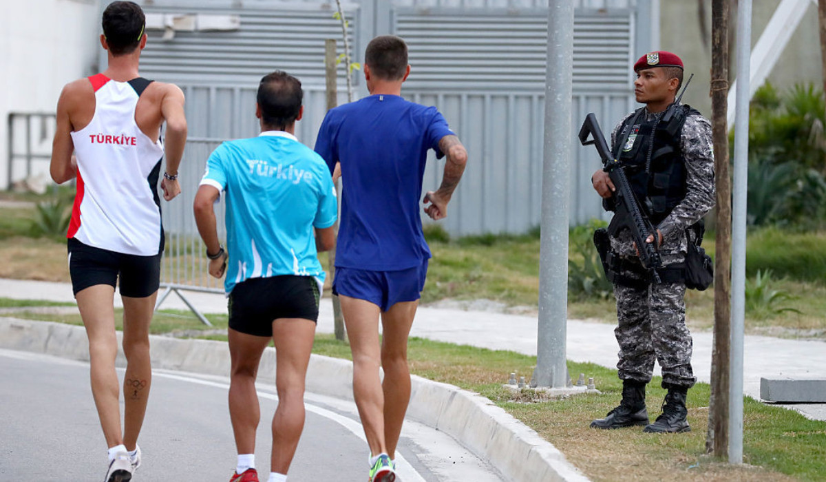 A police officer stands close to some athletes as they walk in the Olympic Village at Rio 2016. GETTY IMAGES