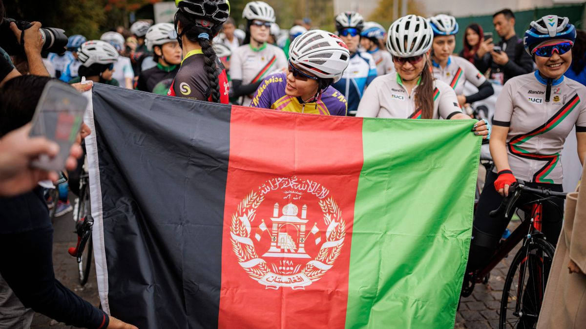 Masomah Ali Zada, the first Afghan cyclist participated in the Olympic Games as a member of the International Olympic Committee refugee team, waits behind an Afghan flag. GETTY IMAGES