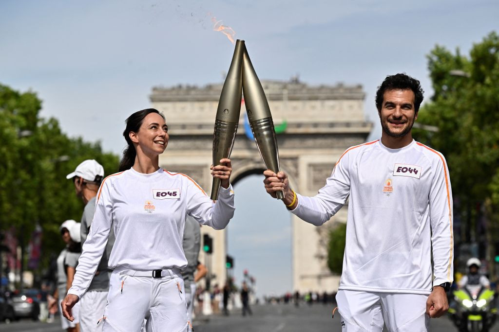 French pastry chef Nina Metayer and French-Israeli singer Amir hold the Olympic flame on the Champs-Elysees avenue, in front of the Arc de Triomphe. GETTY IMAGES