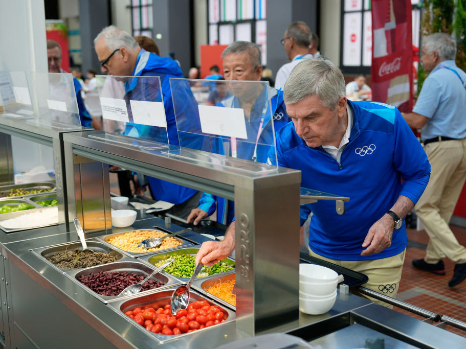 IOC President Thomas Bach tries food from a salad bar while touring at the Olympic Village. GETTY IMAGES