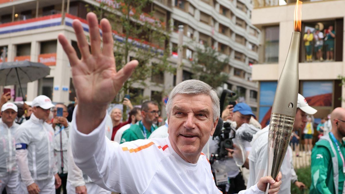 Thomas Bach carries the Olympic torch through the athletes' village