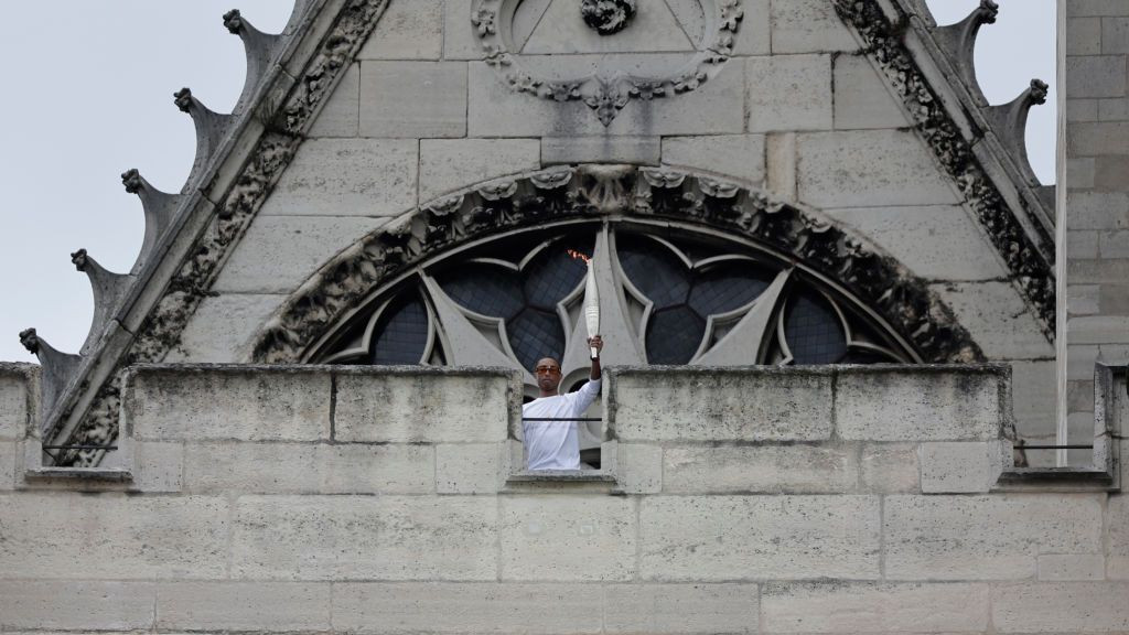 US rapper, artist and designer Pharell Williams stands on the top of the Saint-Denis Cathedral Basilica holding the Olympic Torch during the 2024 Paris Olympic Games Torch Relay, GETTY IMAGES