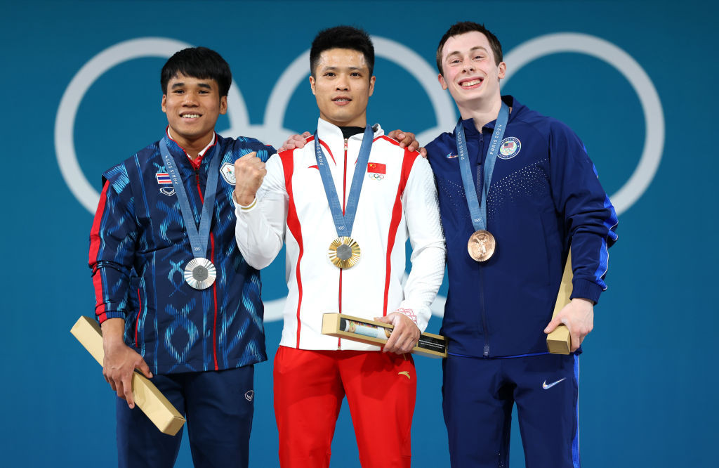 Gold medallist Fabin Li of Team People's Republic of China (C), Silver medallist Theerapong Silachai of Team Thailand (L) and Bronze medallist Hampton Morris of Team United States(R) pose on the podium during the Weightlifting Men's 61kg medal ceremony. GETTY IMAGES