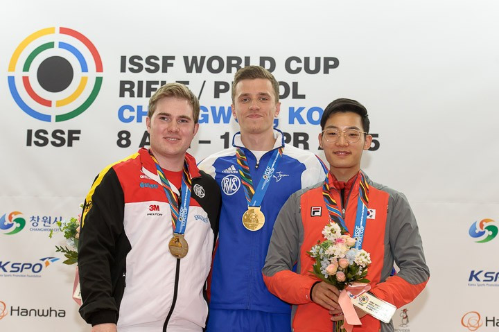 Jean Quiquampoix (centre) celebrates on the podium alongside silver medallist Oliver Geis (left) of Germany and bronze medallist Song Jong Ho (right) of South Korea ©ISSF/Nicolò Zangirolami