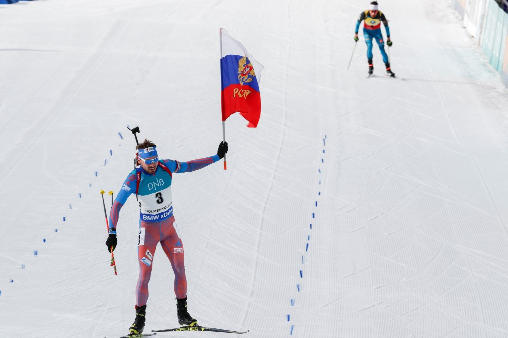 Anton Shipulin waves a Russian flag as he skis over the line in Oslo with Martin Fourcade in the background ©Getty Images