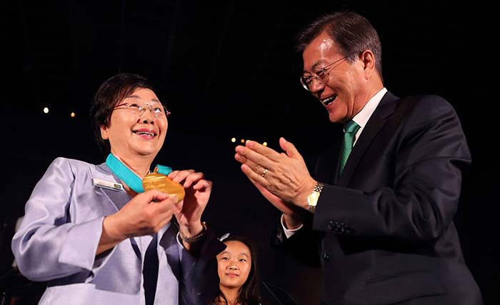 South Korean President Moon Jae-in smiles after he put a gold Pyeongchang 2018 Olympic Games medal around the neck of former speed skater Kim Gui-jin as they were unveiled simultaneously in Seoul and New York City ©Korean Government