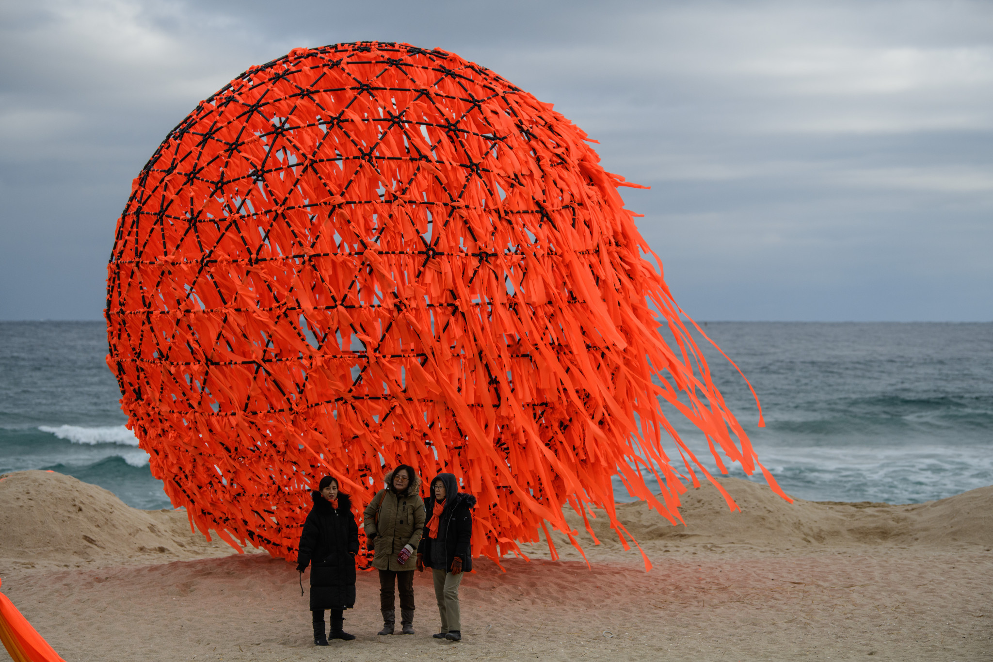 Women stand next to a sculpture on the beach ©Getty Images