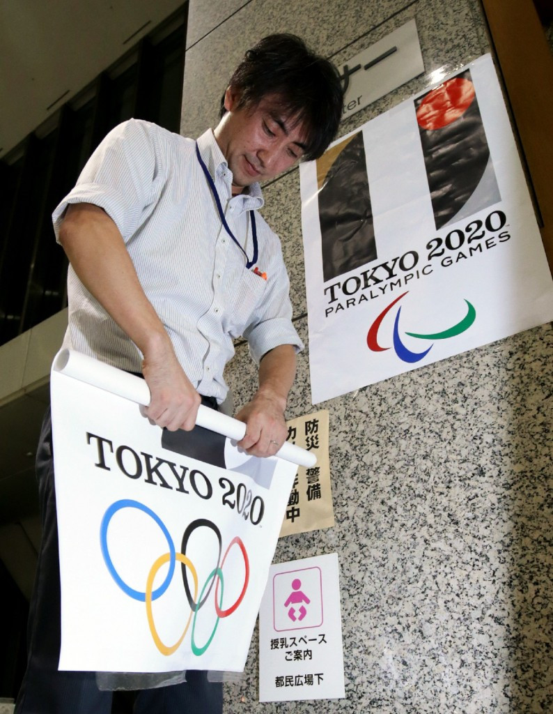 A Tokyo Metropolitan Government officer removes a poster showing the logo of the Tokyo 2020 Olympic Games